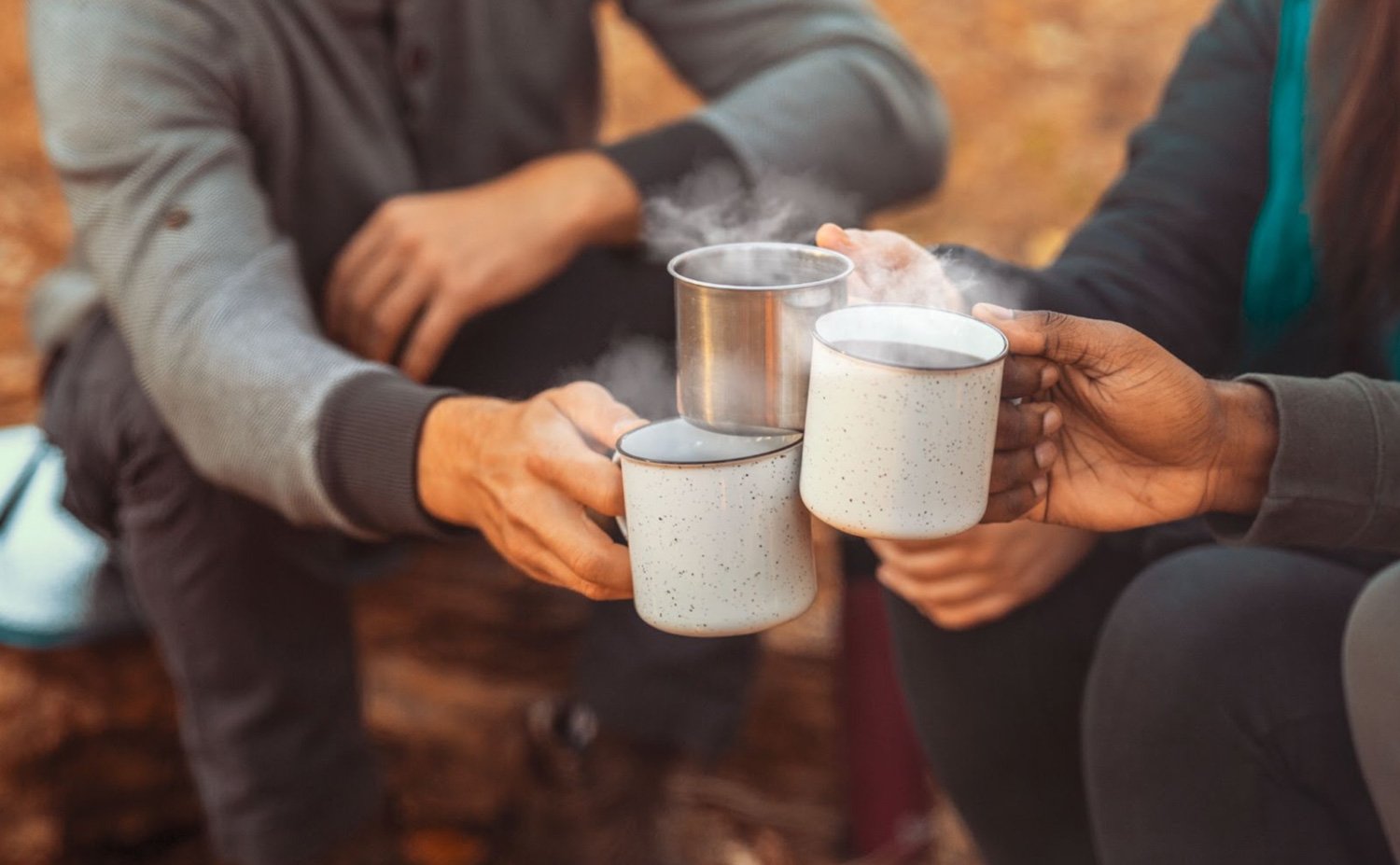 People toasting with their coffee mugs near a campfire
